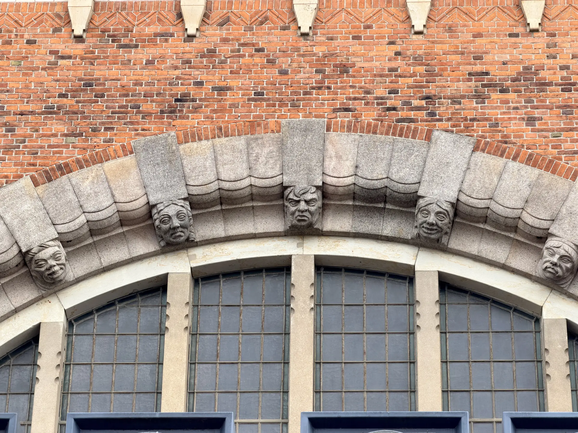Menneskemasker hugget ved siden af et rundbuet vindue.