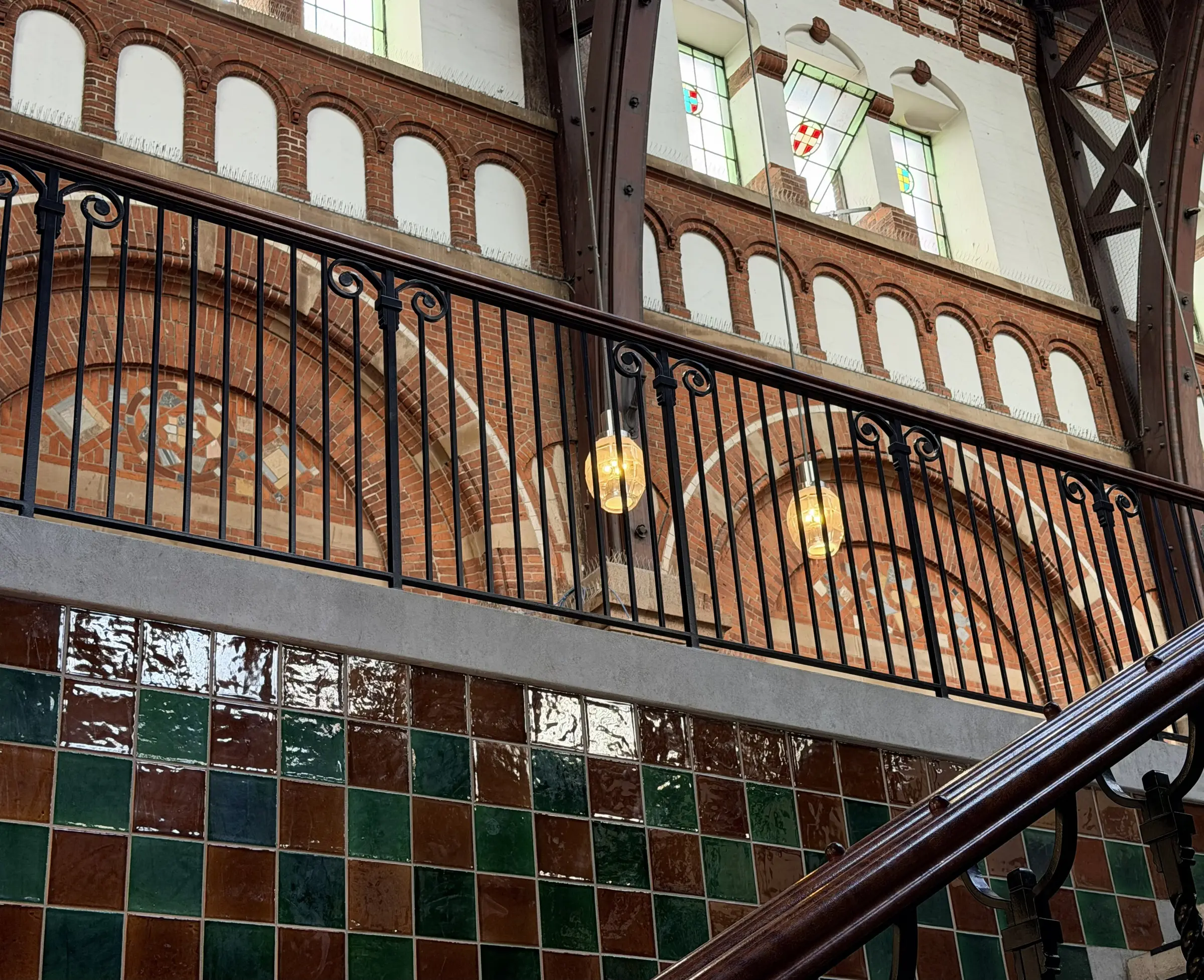 En indvendig trappe med smedejernsbalustrade, træhåndliste og grønne og brune vægfliser.