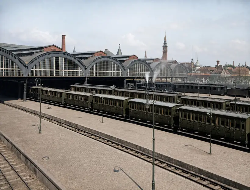 Række af buede glasgavle med mørke buer over perroner med lange rækker af personvogne.