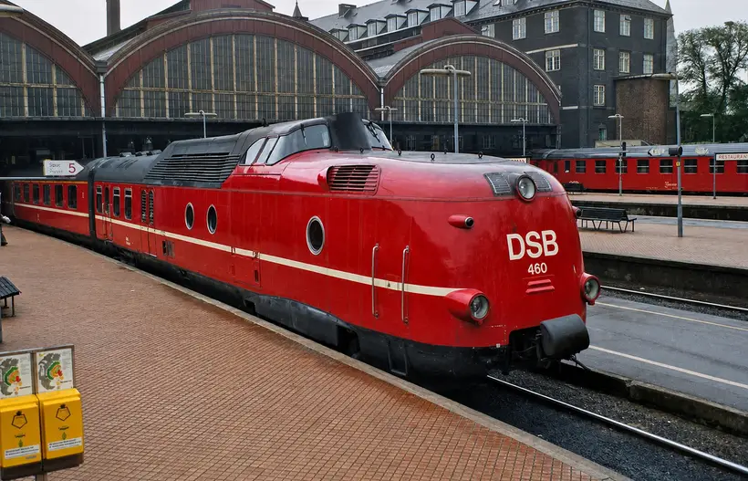 Rødt strømlinet DSB-togsæt ved perronen foran tre buede glasgavle på perronhallerne.