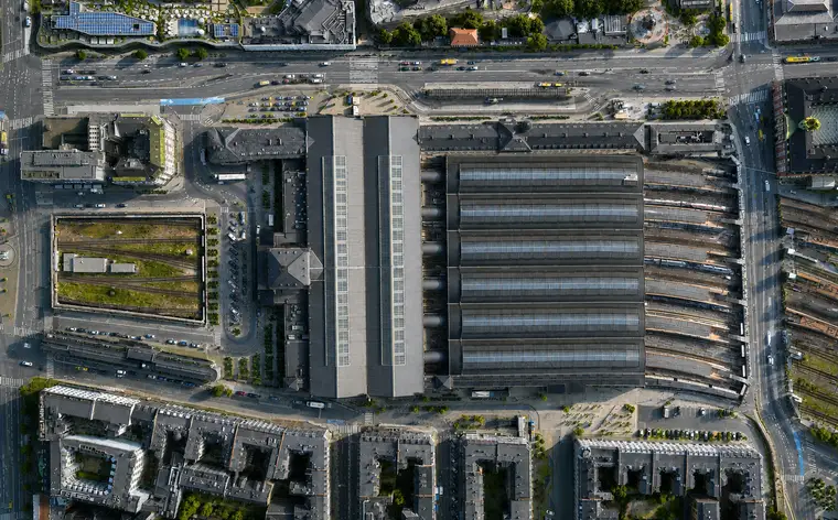 Lodret luftfoto af Københavns Hovedbanegård: seks buede perronhaltage side om side med ovenlys langs hver rygning, hovedhallens tag på tværs af deres nordende, pladsen bagved og et nedsænket sporareal bag støttemure.